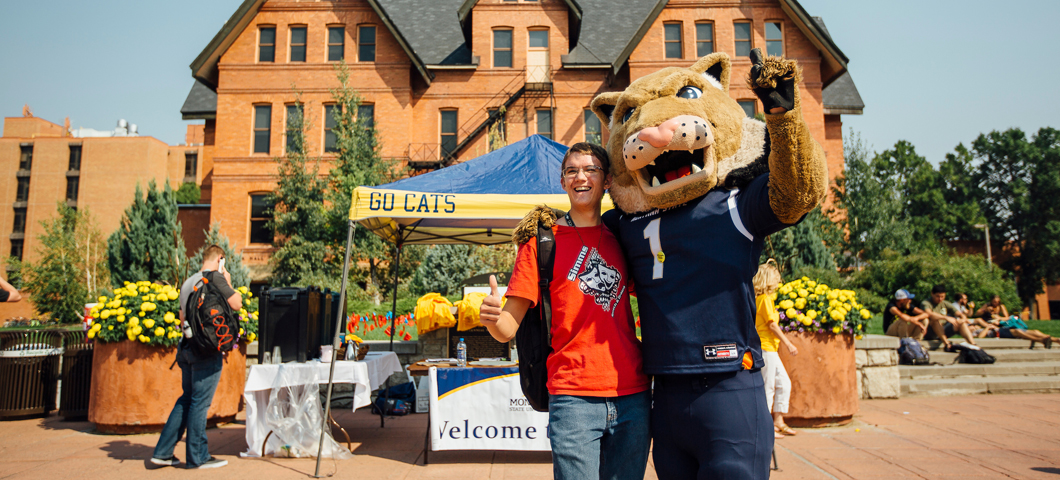 Student posing for a photo with Champ in front of Montana Hall.