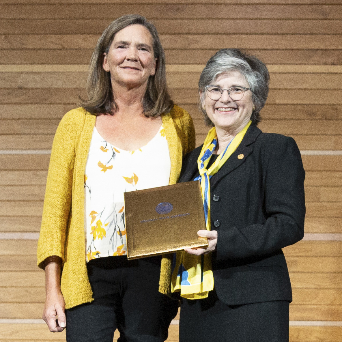 Susan Carstensen stands next to President Waded Cruzado who is holding a gold award