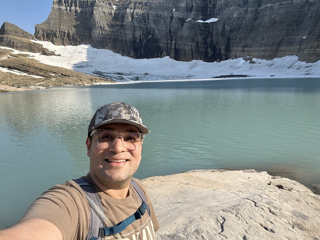 Shahriar outside by a pretty lake with cliffs in the background.