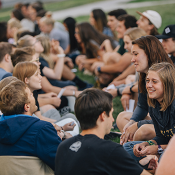 gathering of students sitting in the grass talking to each other