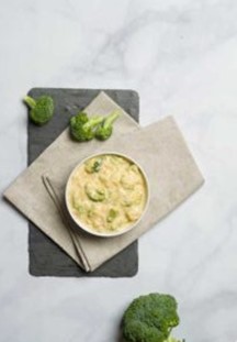 A bowl of Broccoli Cheese Soup next to a crown of broccoli.