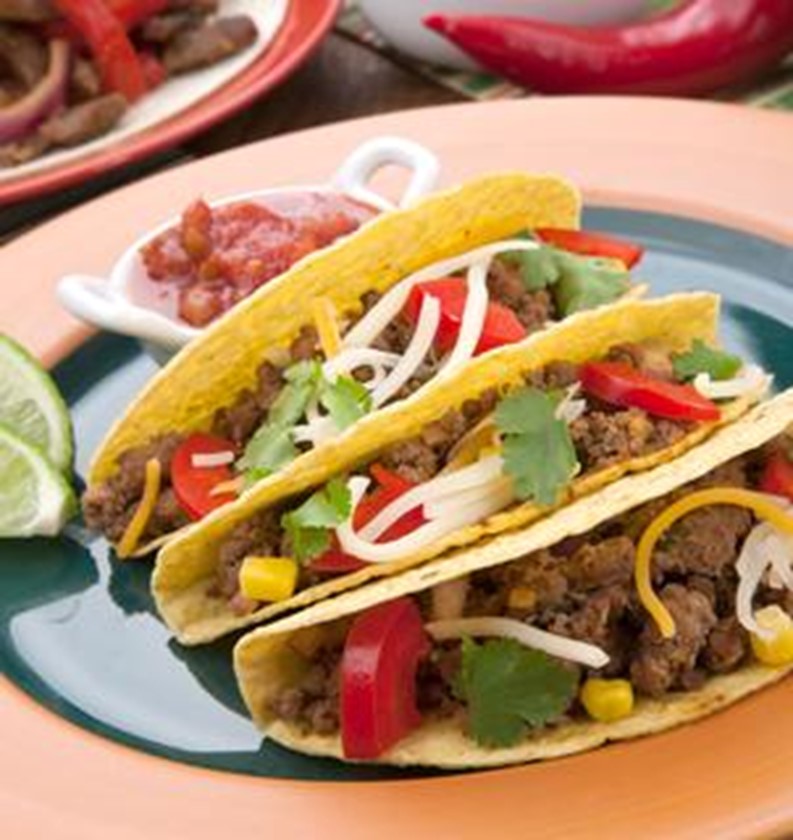 Three tacos on a plate, topped with peppers, cilantro, and cheese.