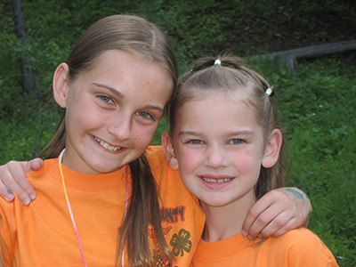Parenting with Confidence Two children wearing matching T-shirts stand outdoors with their arms around each other. Trees, grass, and a wooden fence are visible in the background.