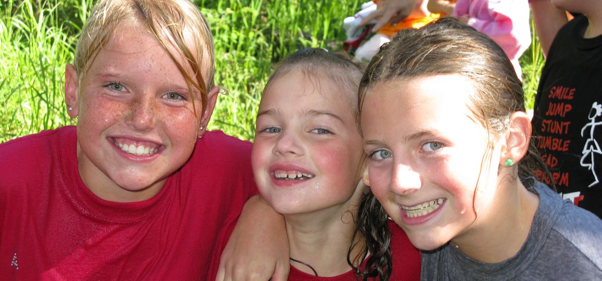 Three children outdoors pose together during summer play.