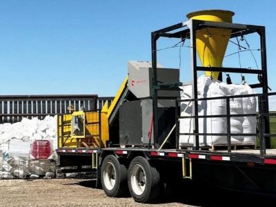 Agricultural Plastics are Recyclable Trailer-mounted agricultural plastics processing equipment parked outdoors beside large bags of collected plastic material.