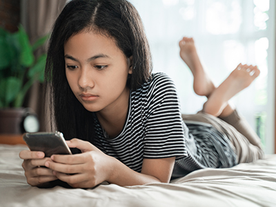 Smartphone Use by Teenagers A young person is propped up on their elbows looking at a smartphone.