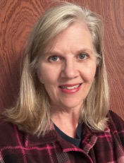 Portrait of a woman with blonde hair wearing a black and collared shirt. Wood background.