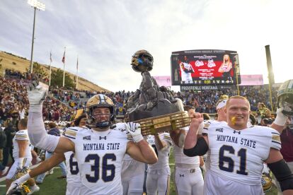 Montana State football players celebrate holding a trophy after a game at Washington-Grizzly Stadium.