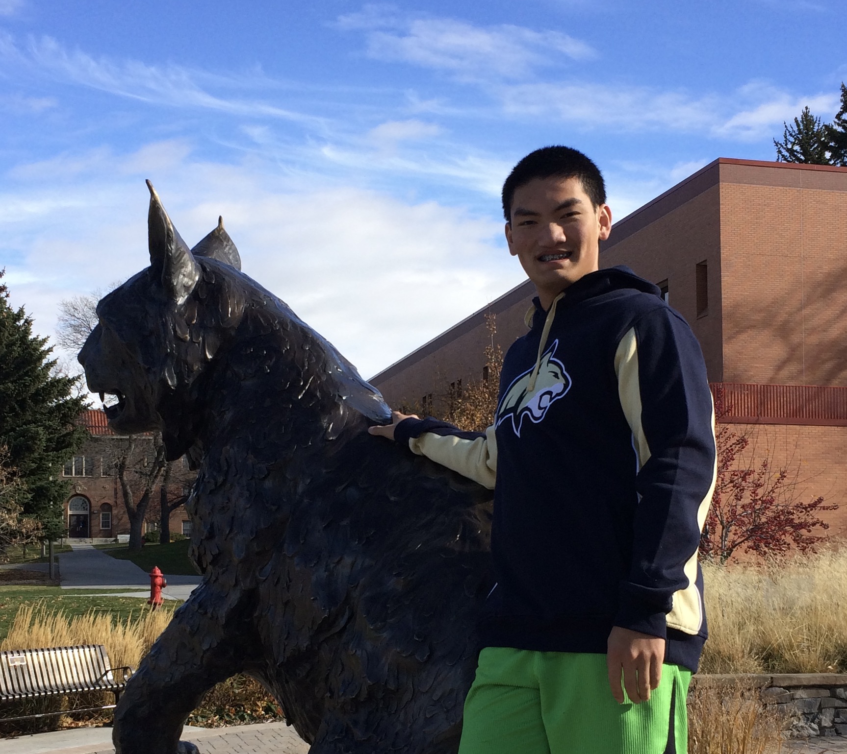 Male student posing with hand on bobcat statue