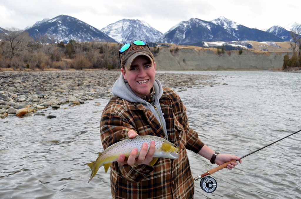 Male student holding a fish in a beautiful mountain river